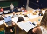 Students sit in a lecture theatre with open notebooks and laptops