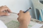 close up of a have holding a pencil and marking answers on a multiple choice questions exam
