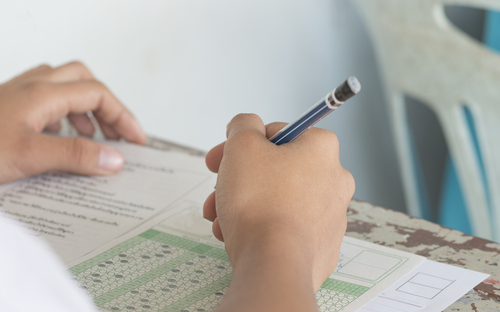 close up of a have holding a pencil and marking answers on a multiple choice questions exam