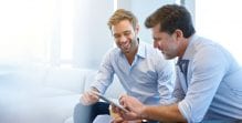 Two men sit next to each other and look at a document