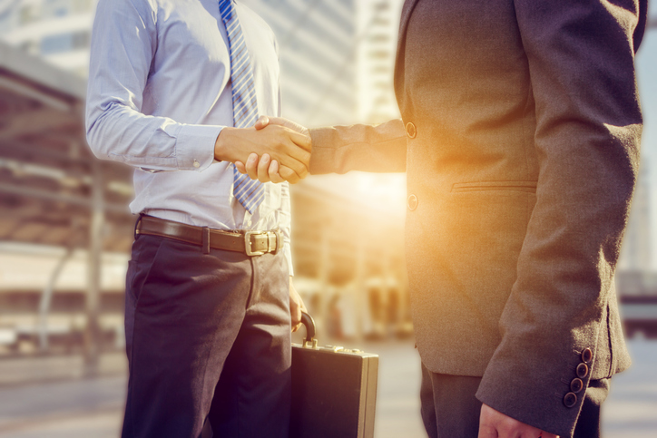 Tow men in business attire shaking hands outside an office building as the sun sets