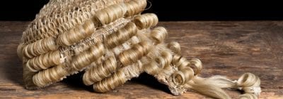 A blonde barrister wig rests on a wooden desk