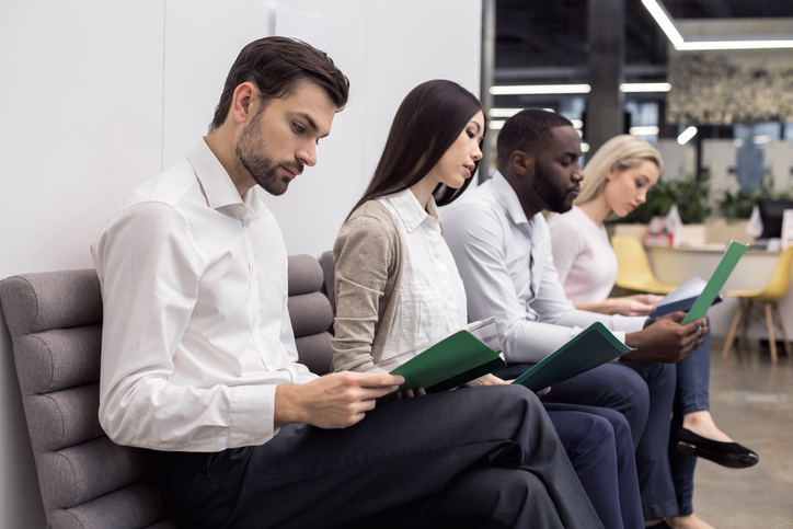 Young people in an office waiting room. They are sitting, holding CVs and waiting for job interview.