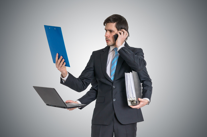 Multitasking man at work is calling with phone, reading report, working with laptop and holding office documents.