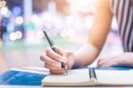 Student writing in a notebook at her desk learning about the LNAT