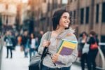Young woman holding school books walking down the street with a smile on her face