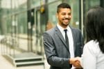 A man in a grey suit shakes the hand of a woman wearing a white top