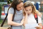 A girl comforts her friend as she looks at a piece of paper and looks upset