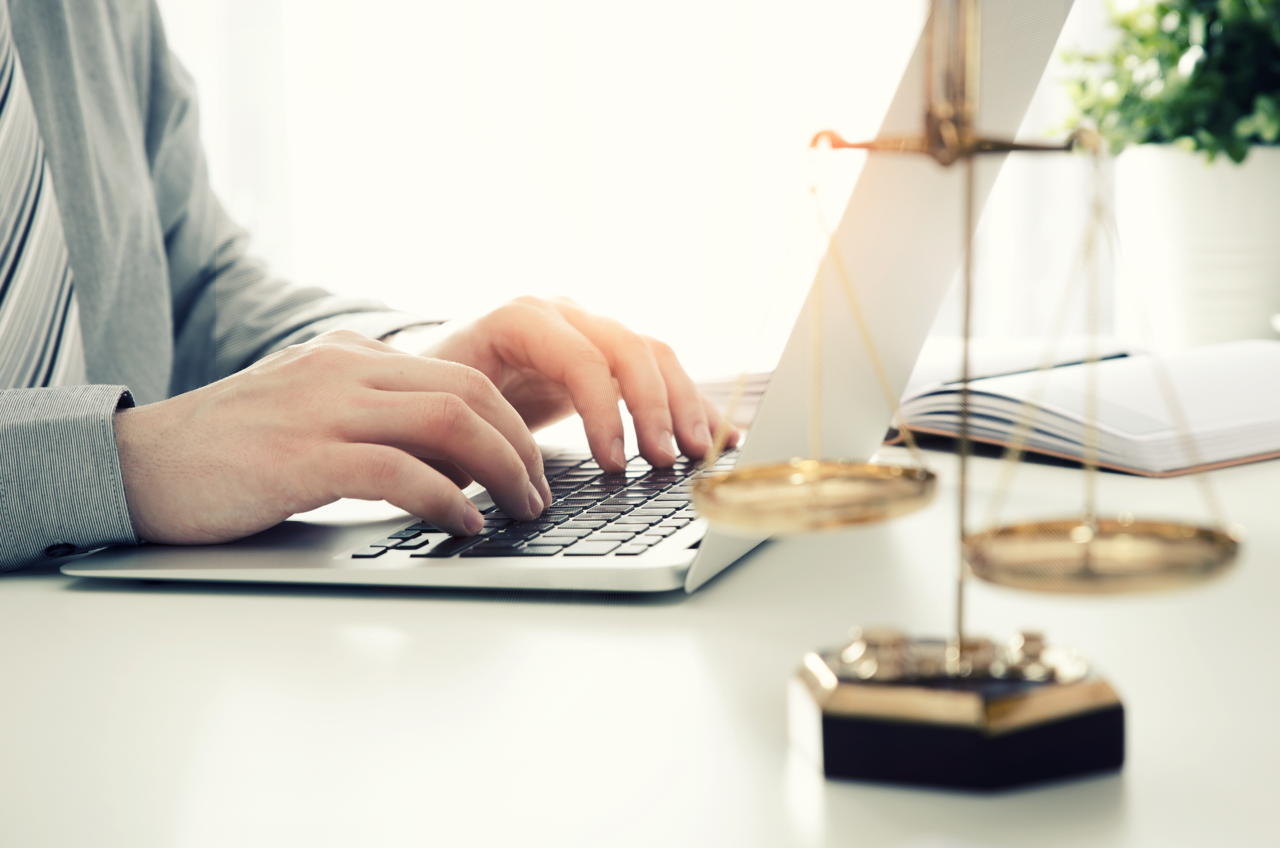 A woman types on her laptop and there is a set of balance scales to her right hand side