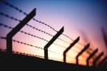 A barbed wire fence is seen against a purple sunset