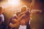 Three female football players hug each other to celebrate their achievements on the playing field at sunset