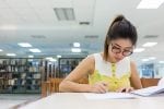 Young woman writing something at a desk in a library