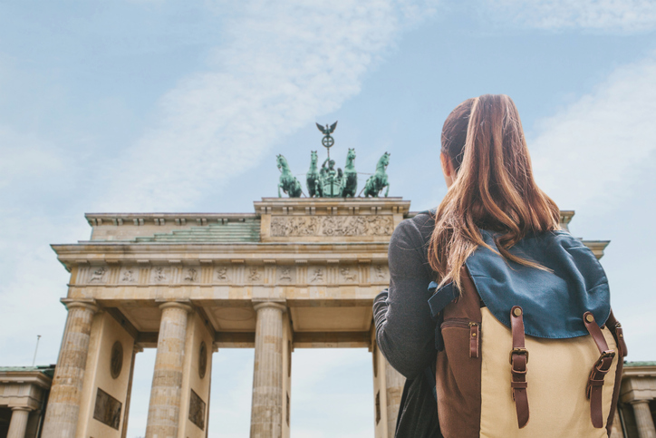 A tourist girl with a backpack on stands looking up at the Brandenberg Gate in Berlin, Germany