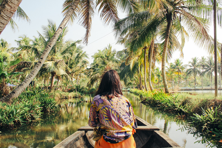 A young woman kayaks down a river surrounded by palm trees