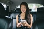 A girl sits in the back of a car looking down at her mobile phone