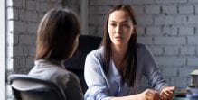 A woman sits at a table facing another woman