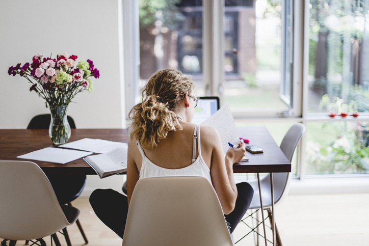 Young woman with back to camera studying at kitchen table