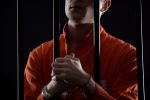 Criminal in orange jumpsuit and handcuffs behind bars
