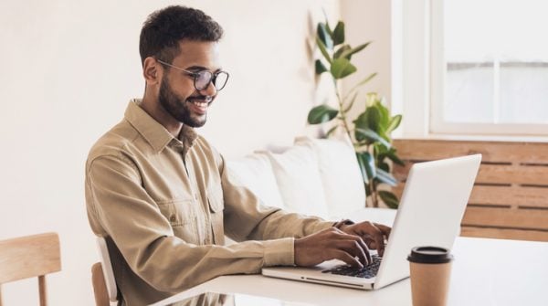 Young male student at his laptop smiling into the webcam