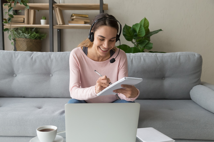 Woman sitting in front of her laptop taking notes on a pad of paper