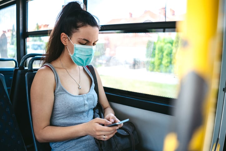 Woman on a bus wearing a face mask while texting