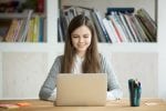 A girl sits at a desk with her laptop open in front of her
