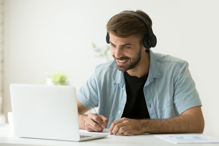 A man sits with headphones on in front of his open white laptop