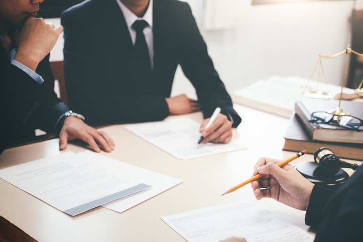 Lawyers sit around a table with documents on the table in front of them